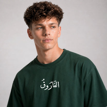 Man wearing a dark green sweatshirt with Arabic text on a gray background