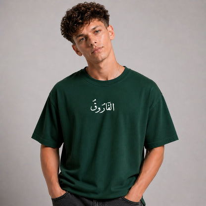 Person wearing a green t-shirt with Arabic text on a gray background