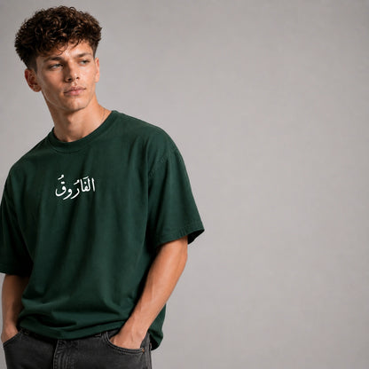Man wearing a green t-shirt with Arabic text on a gray background
