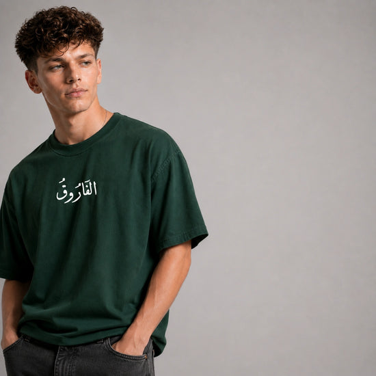 Man wearing a green t-shirt with Arabic text on a gray background