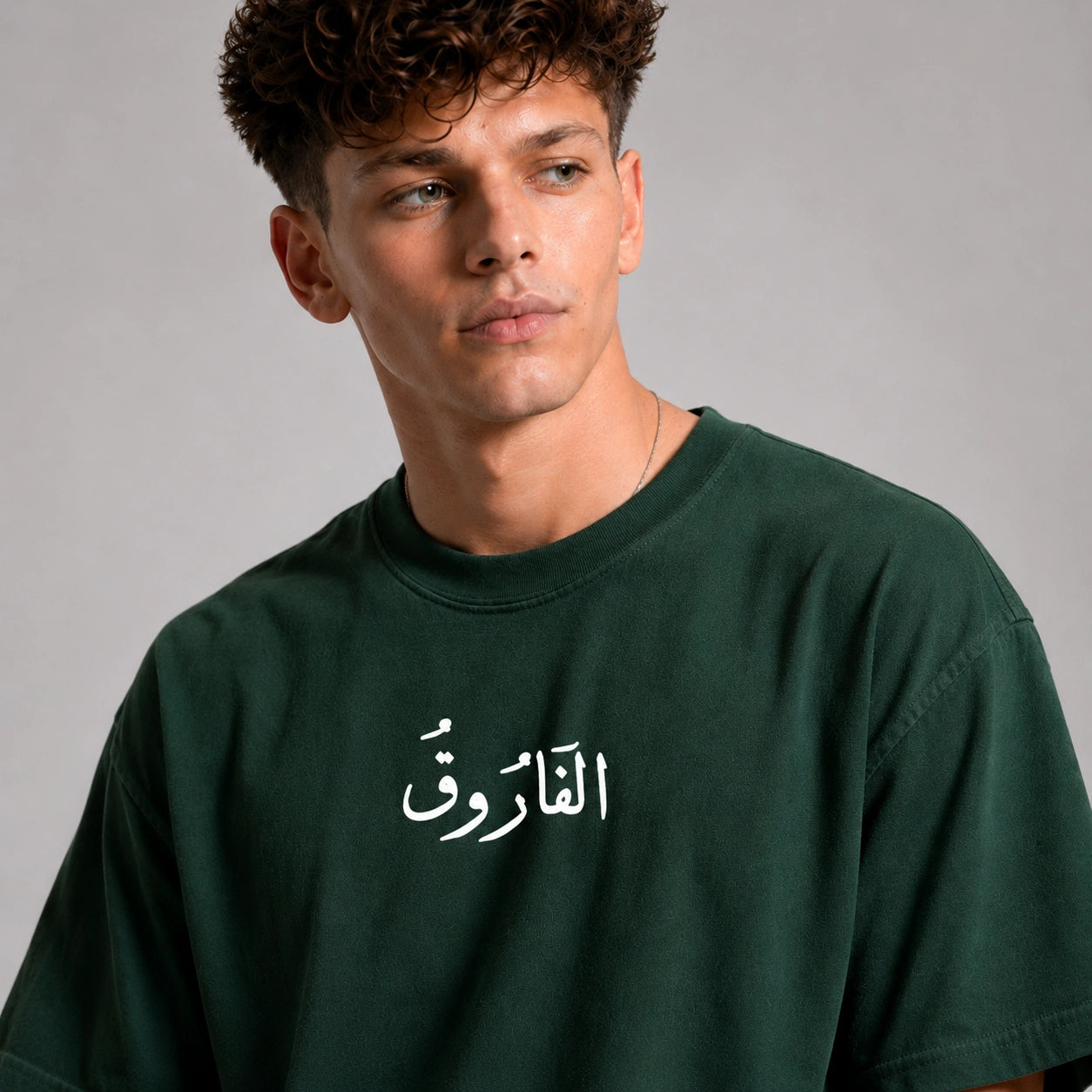 Man wearing a green t-shirt with Arabic text on a gray background