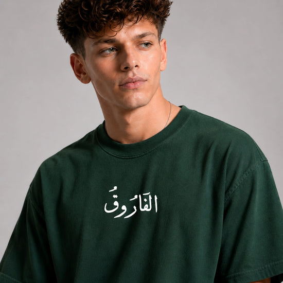 Man wearing a green t-shirt with Arabic text on a gray background