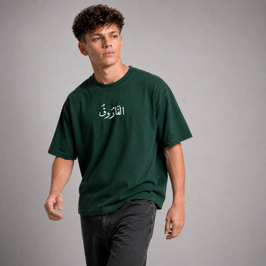 Person wearing a green t-shirt with Arabic text on a gray background