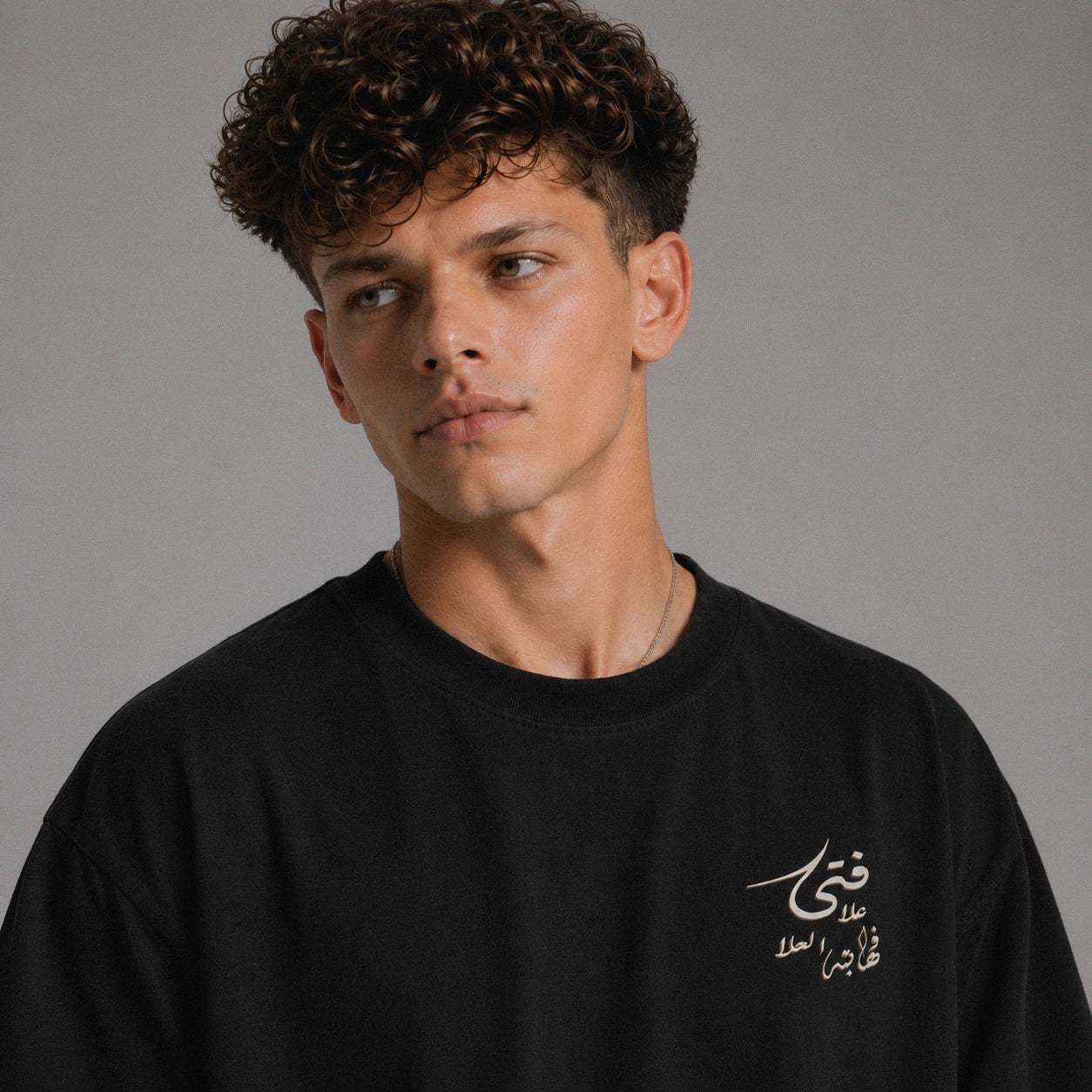 Man wearing a black sweatshirt with Arabic text on a gray background