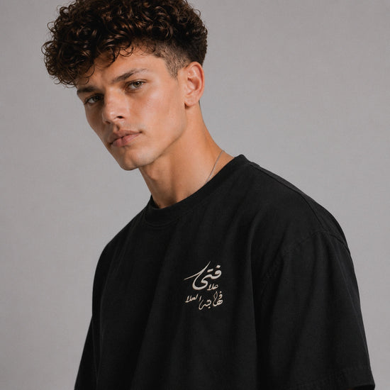 Man wearing a black t-shirt with Arabic text on a gray background
