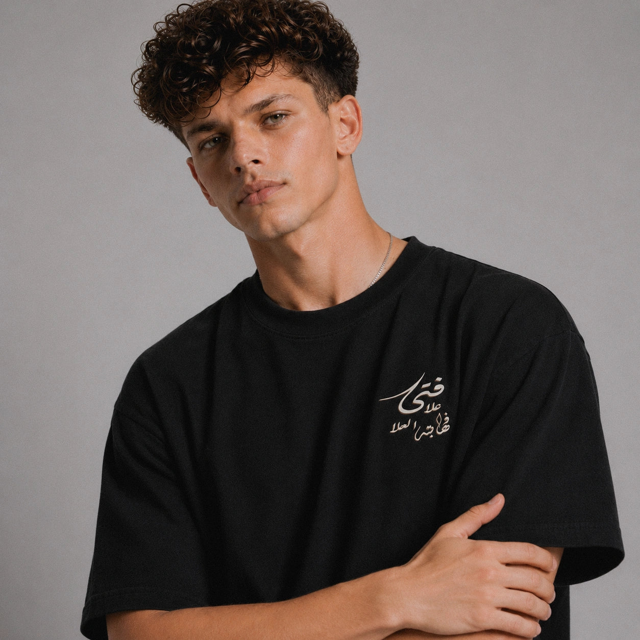 Man wearing a black t-shirt with Arabic text on a gray background