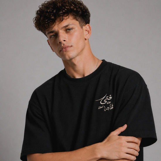 Man wearing a black t-shirt with Arabic text on a gray background