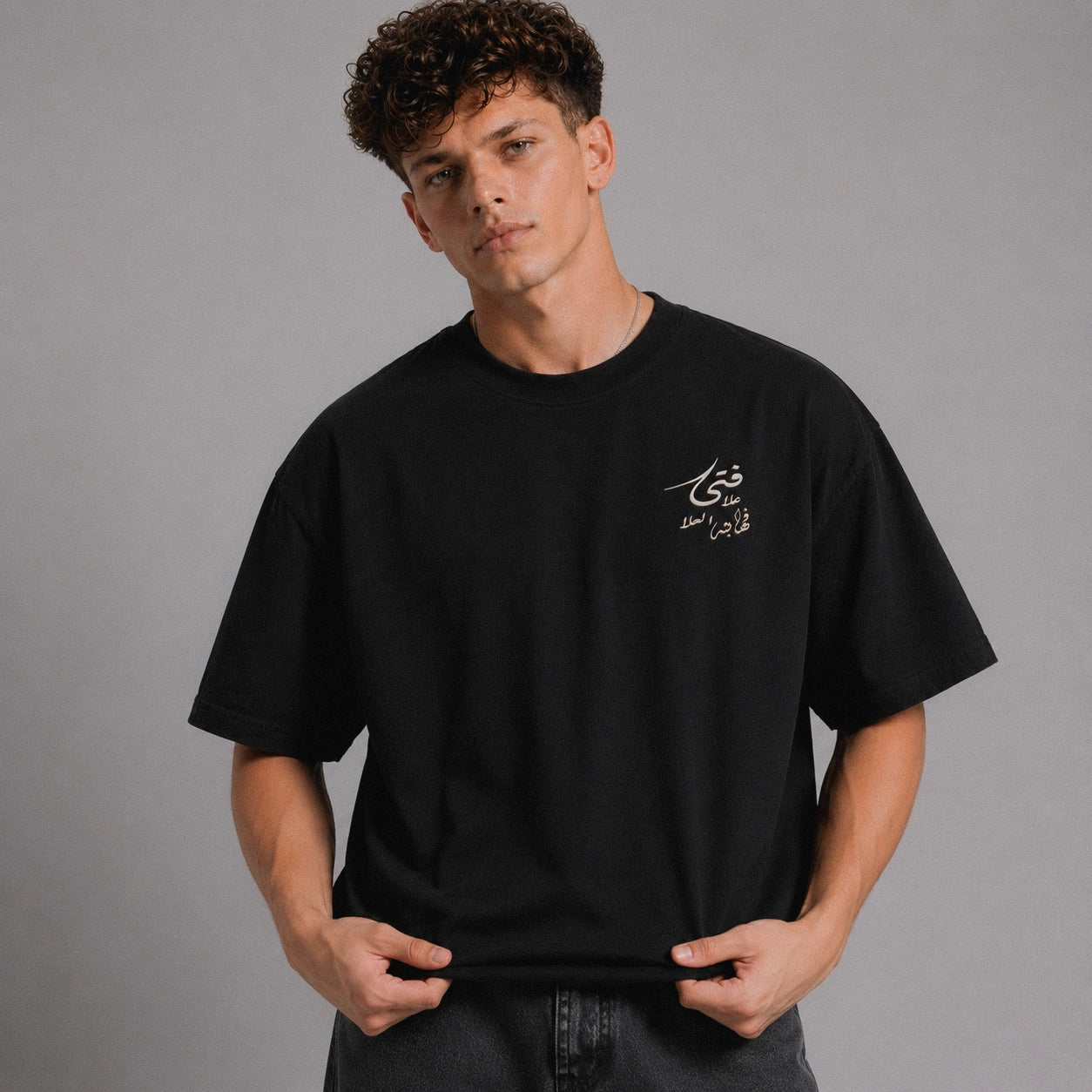Person wearing a black t-shirt with Arabic text on a gray background