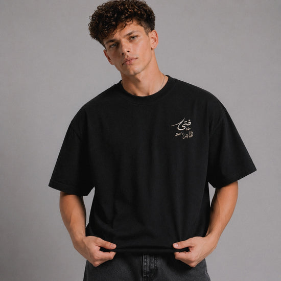 Person wearing a black t-shirt with Arabic text on a gray background
