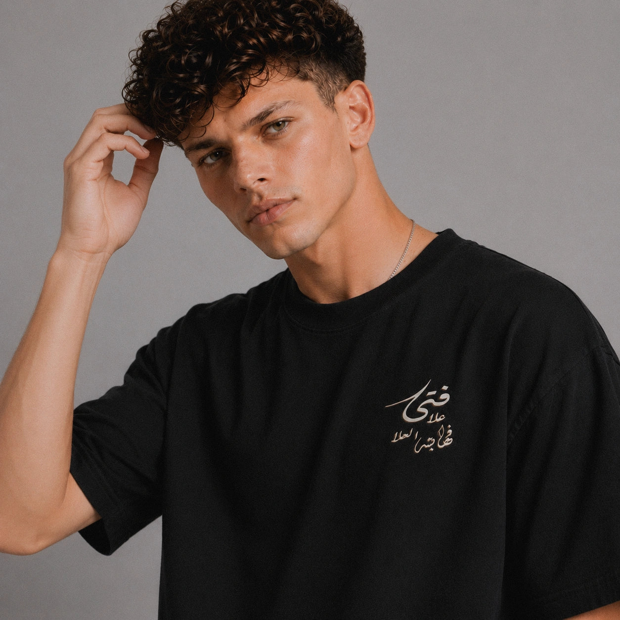 Man wearing a black t-shirt with Arabic text against a gray background