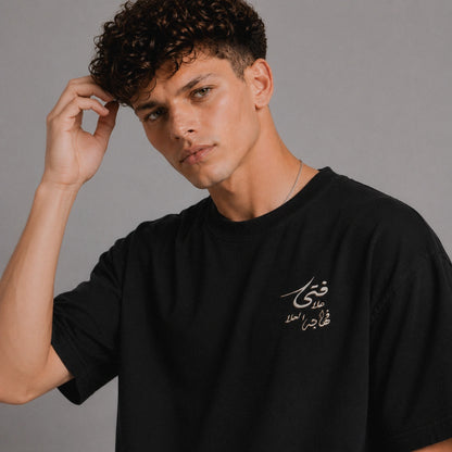 Man wearing a black t-shirt with Arabic text against a gray background