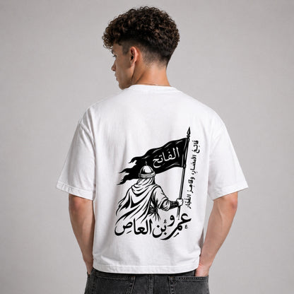 Person wearing a white t-shirt with a black graphic and Arabic text on the back, standing against a gray background.