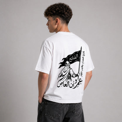 Person wearing a white t-shirt with Arabic text and graphic design on the back, standing against a gray background.