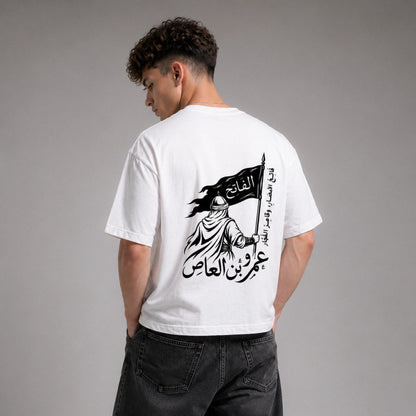 Person wearing a white t-shirt with Arabic text and design on the back, standing against a gray background.
