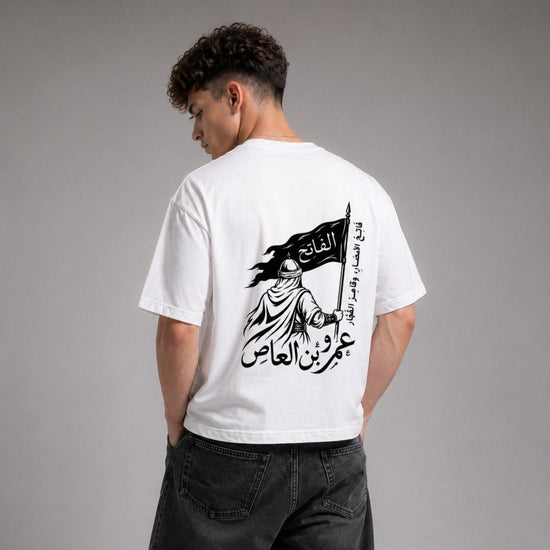 Person wearing a white t-shirt with Arabic text and design on the back, standing against a gray background.