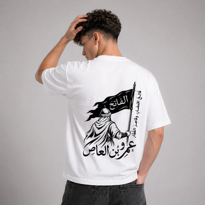 Person wearing a white t-shirt with Arabic text and graphic design on the back, standing against a gray background.