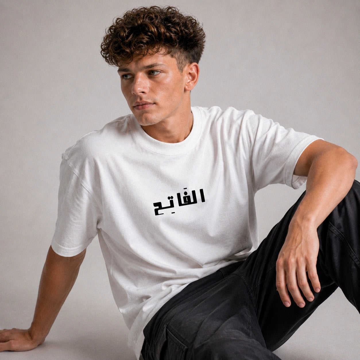 Person wearing a white t-shirt with Arabic text on a plain background