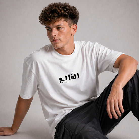 Person wearing a white t-shirt with Arabic text on a plain background