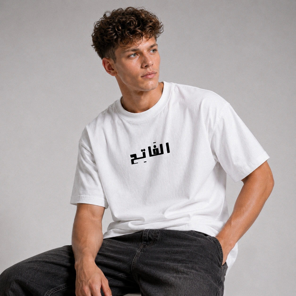 Person wearing a white t-shirt with Arabic text on a gray background
