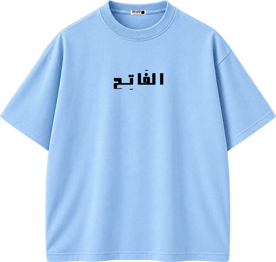 A light blue short-sleeve crewneck t-shirt with black Arabic text printed across the chest, displayed on a clean white background.