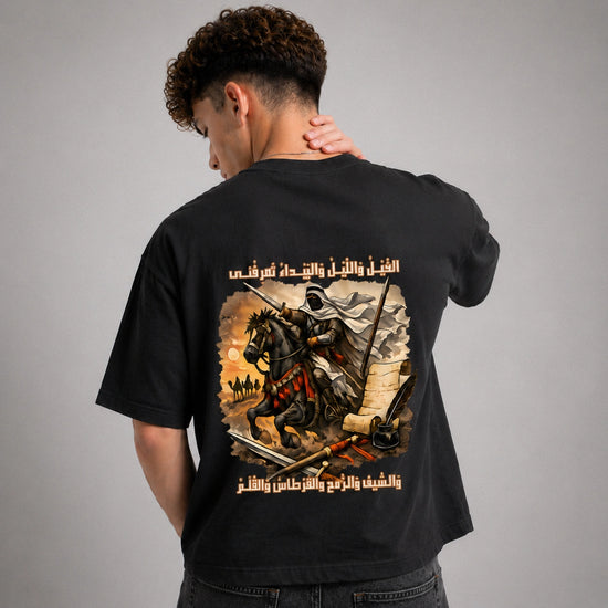 Person wearing a black t-shirt with a graphic design on the back, featuring a warrior on horseback and Arabic text.
