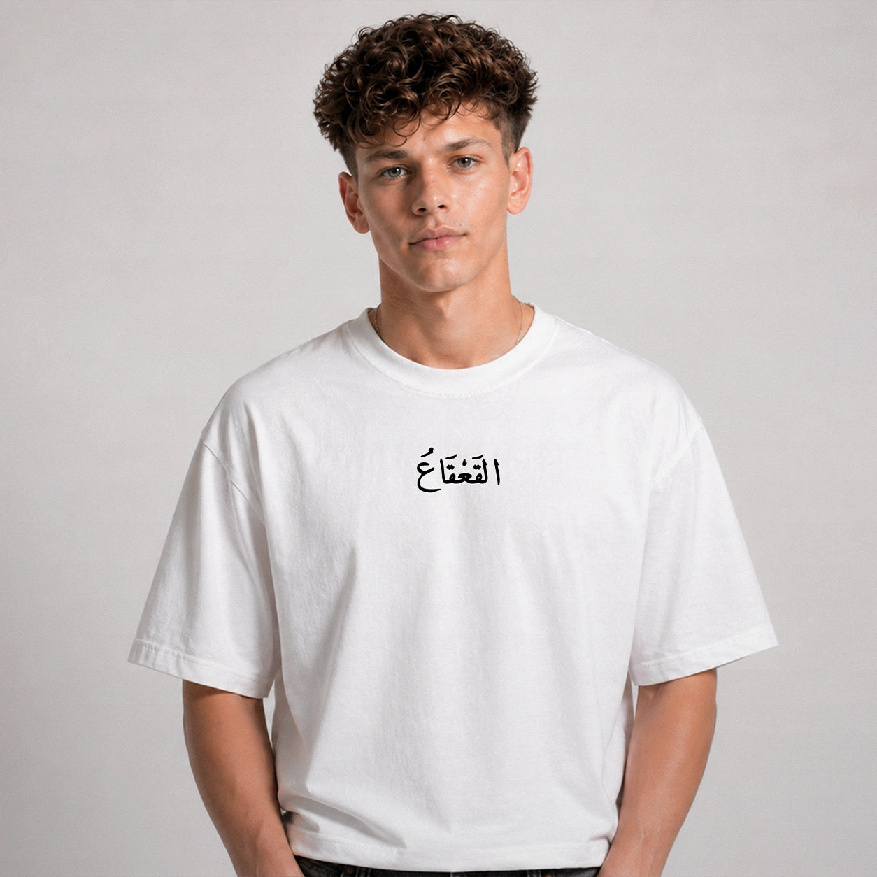 Person wearing a white t-shirt with Arabic text on a plain background