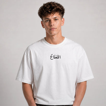 Person wearing a white t-shirt with Arabic text on a plain background