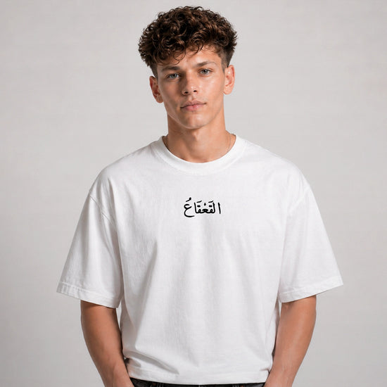 Person wearing a white t-shirt with Arabic text on a plain background