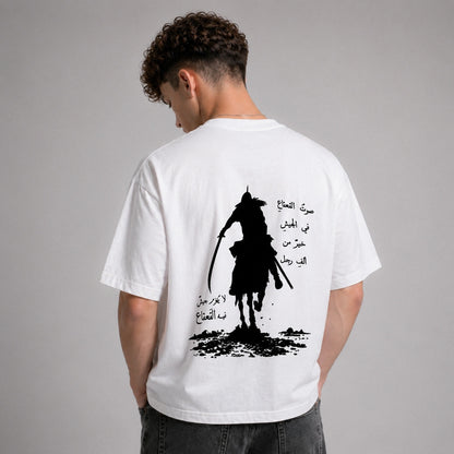 Person wearing a white t-shirt with a black silhouette design and Arabic text on the back, against a gray background.