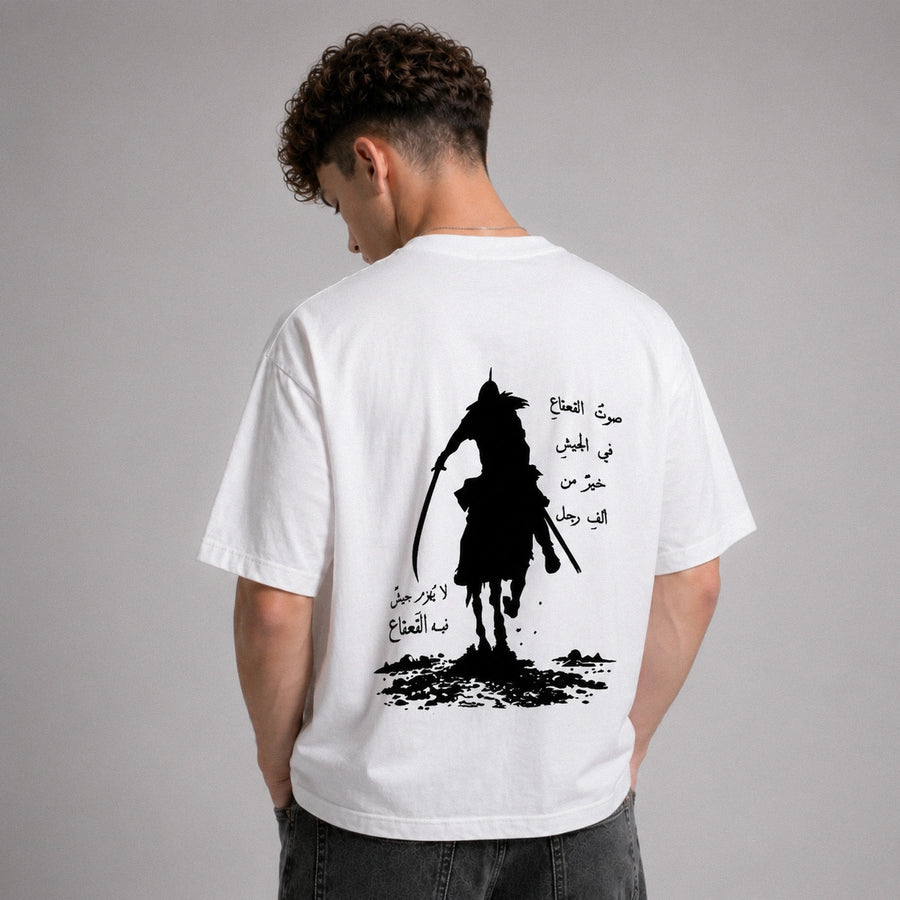 Person wearing a white t-shirt with a black silhouette design and Arabic text on the back, against a gray background.