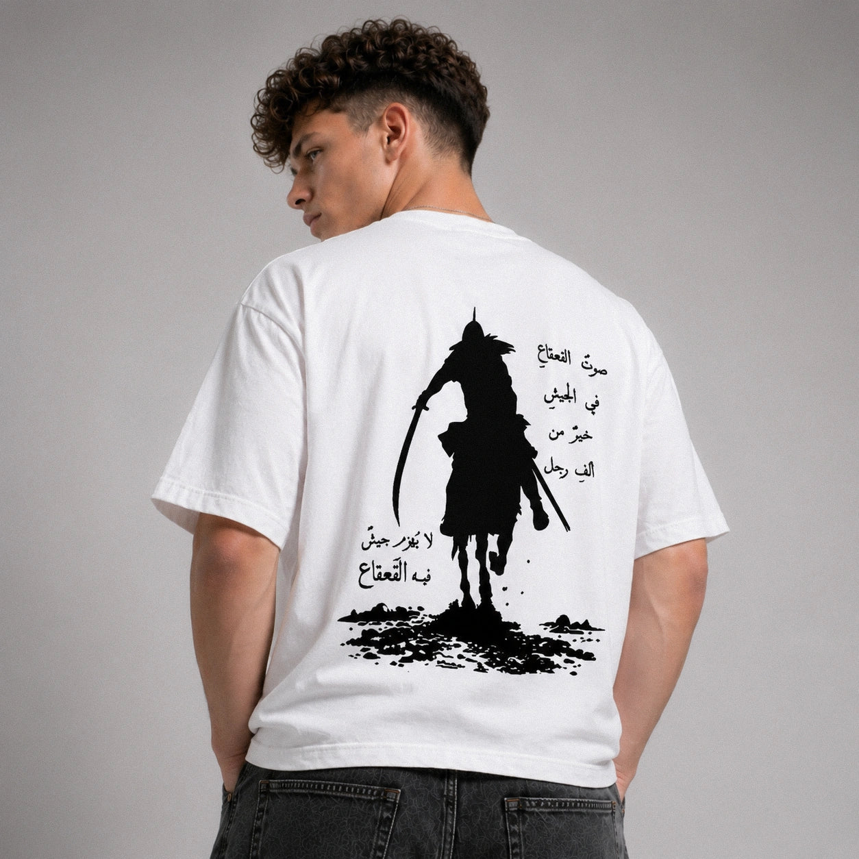 Person wearing a white t-shirt with a black silhouette design and Arabic text on the back.