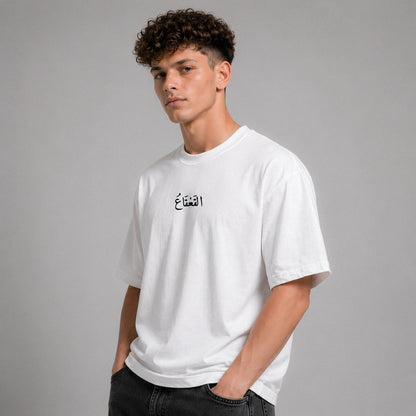 Man wearing a white t-shirt with Arabic text on a gray background