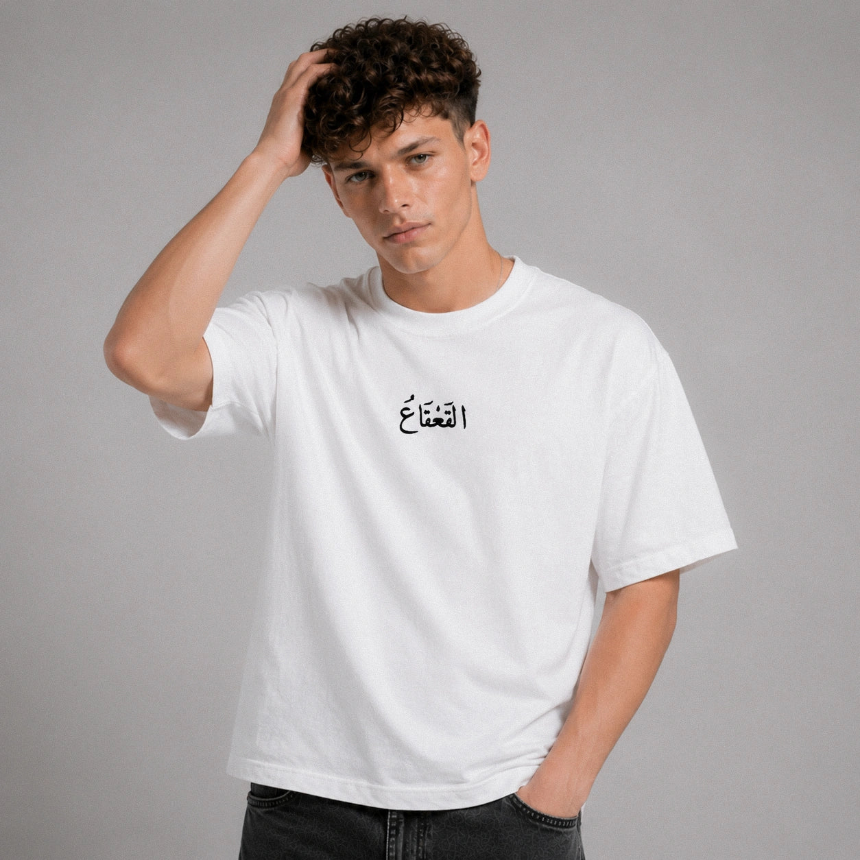 Person wearing a white t-shirt with Arabic text on a gray background