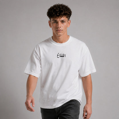 Person wearing a white t-shirt with Arabic text on a plain background