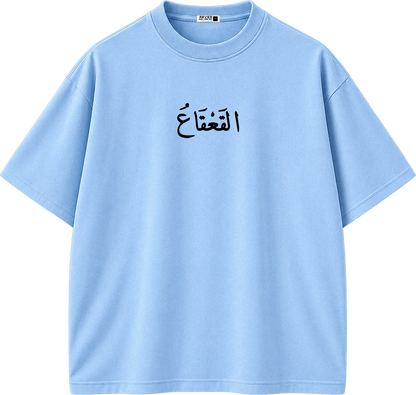 A light blue short-sleeve crewneck t-shirt with black Arabic calligraphy printed on the center chest, displayed on a clean white background.