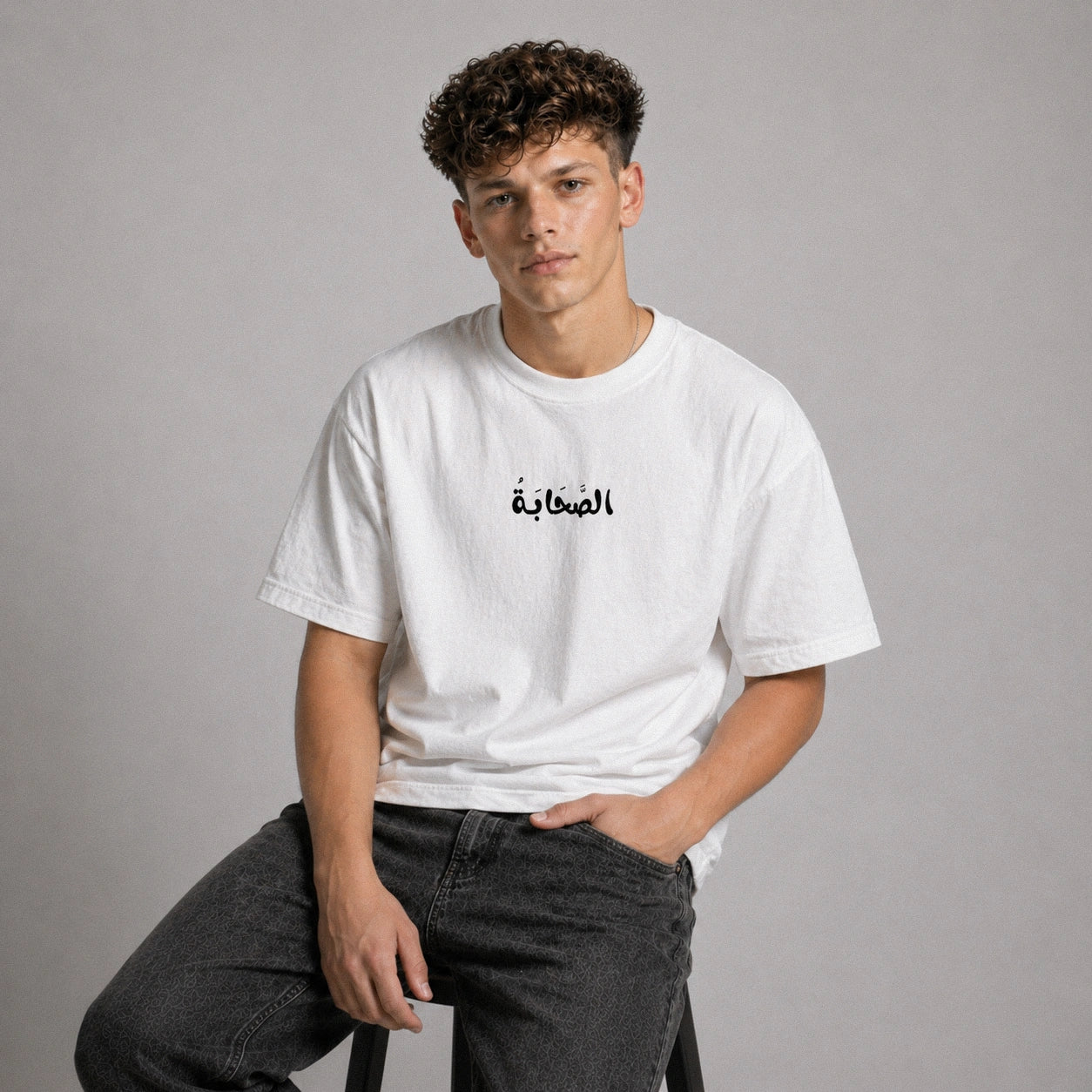 Person wearing a white t-shirt with Arabic text on a gray background