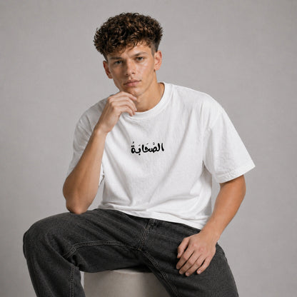 Person wearing a white t-shirt with Arabic text sitting on a gray background