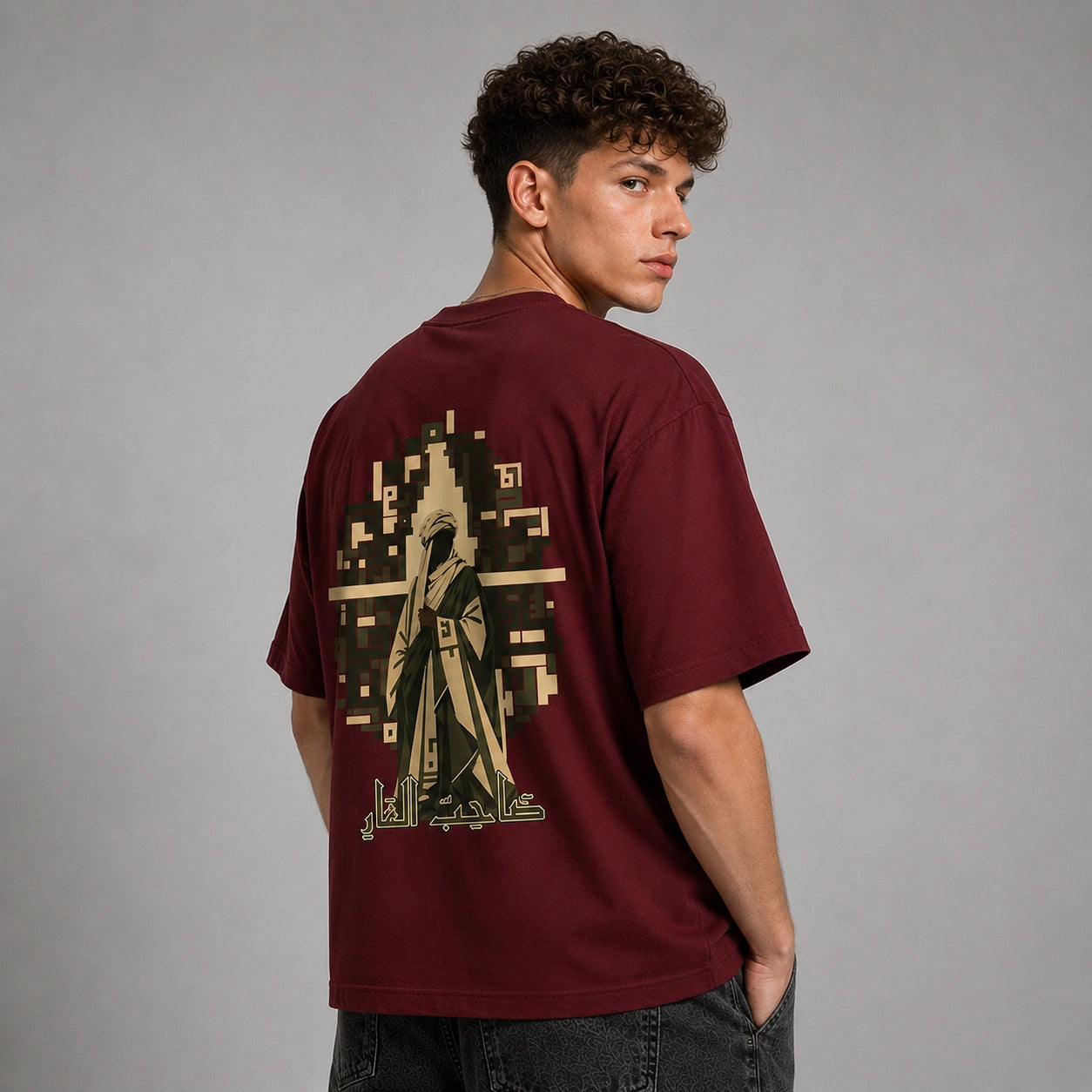 A man wearing a maroon t-shirt with a large graphic print on the back, photographed from behind against a neutral gray studio background.