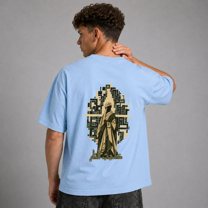 A man wearing a light blue t-shirt, viewed from the back. The shirt features a large graphic print of a robed figure inside a geometric arch design in olive green, beige, and black.