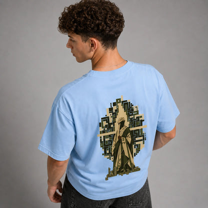 A man wearing a light blue t-shirt, viewed from the back. The shirt features a large graphic print of a hooded figure in a trench coat set against a pixelated tree silhouette.