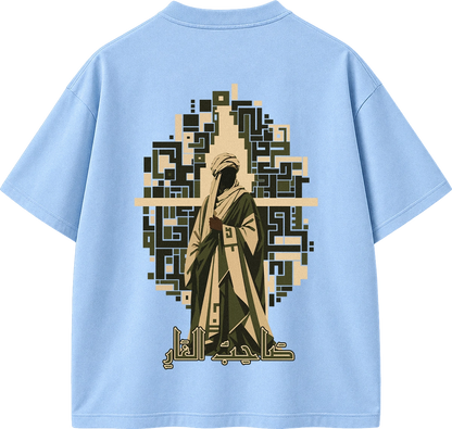 A light blue short-sleeve t-shirt shown from the back, featuring a large graphic print of a robed figure with Arabic calligraphy and a geometric pixelated arch in beige, olive green, and black.