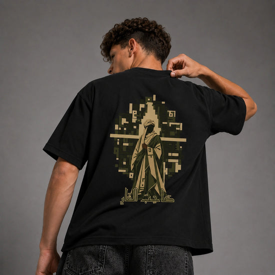 A man wearing a black t-shirt from the back, showing a large graphic print of a robed figure in a pixelated geometric design in olive green and beige.