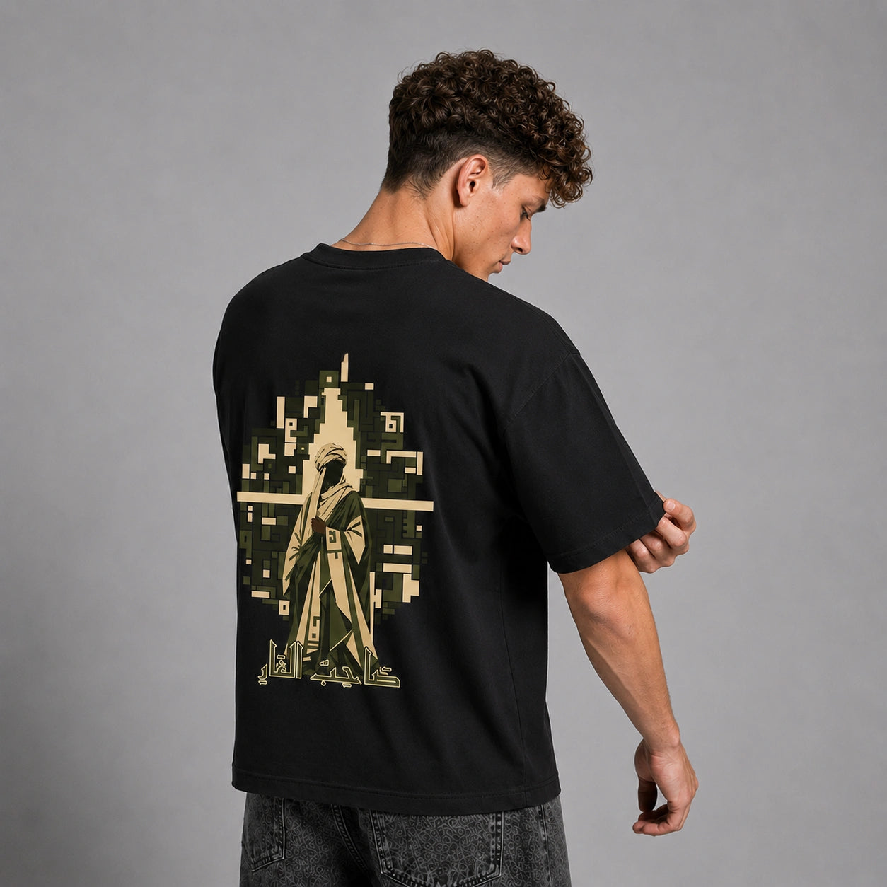 A man wearing a black t-shirt with a large pixelated graphic on the back, shown from behind against a gray studio background.