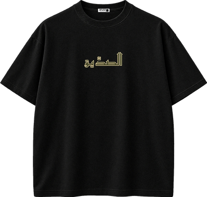 A black short-sleeve crewneck t-shirt with gold Arabic calligraphy printed across the chest, displayed on a clean white background.