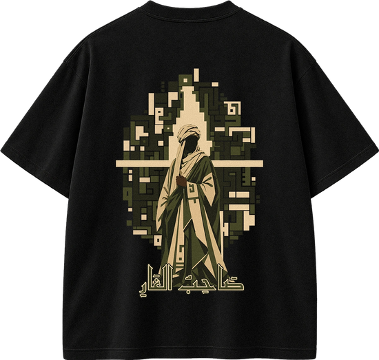 A black short-sleeve t-shirt shown flat against a white background, featuring a large graphic print on the back. The graphic depicts a stylized figure in traditional robes in beige and olive green tones, framed by a pixelated arch, with Arabic calligraphy printed below.