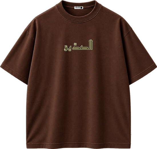 A brown short-sleeve crewneck t-shirt with Arabic calligraphy printed in light green on the chest, displayed on a clean white background.
