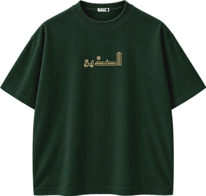 A dark green short-sleeve crewneck t-shirt with gold Arabic calligraphy printed across the chest, displayed on a clean white background.