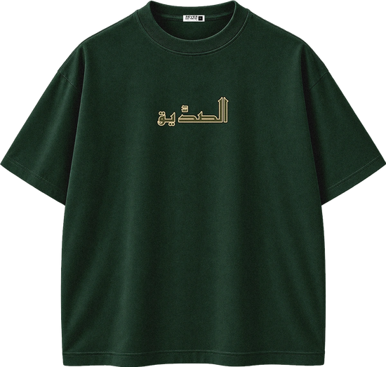 A dark green short-sleeve crewneck t-shirt with gold Arabic calligraphy printed across the chest, displayed on a clean white background.