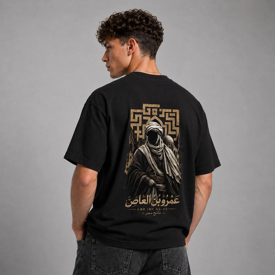 A man wearing a black t-shirt with a large gold graphic print on the back, shown from behind against a neutral gray studio background.