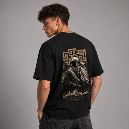 A man wearing a black t-shirt with a large graphic print on the back, photographed from behind against a neutral gray studio background.